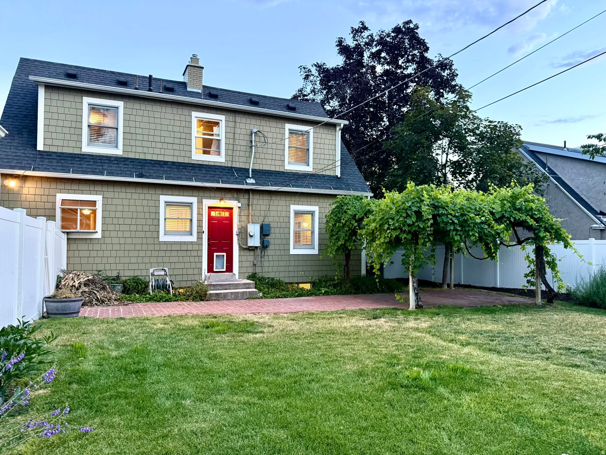 Expansive backyard featuring a manicured lawn, brick patio, and mature vine-covered arbor