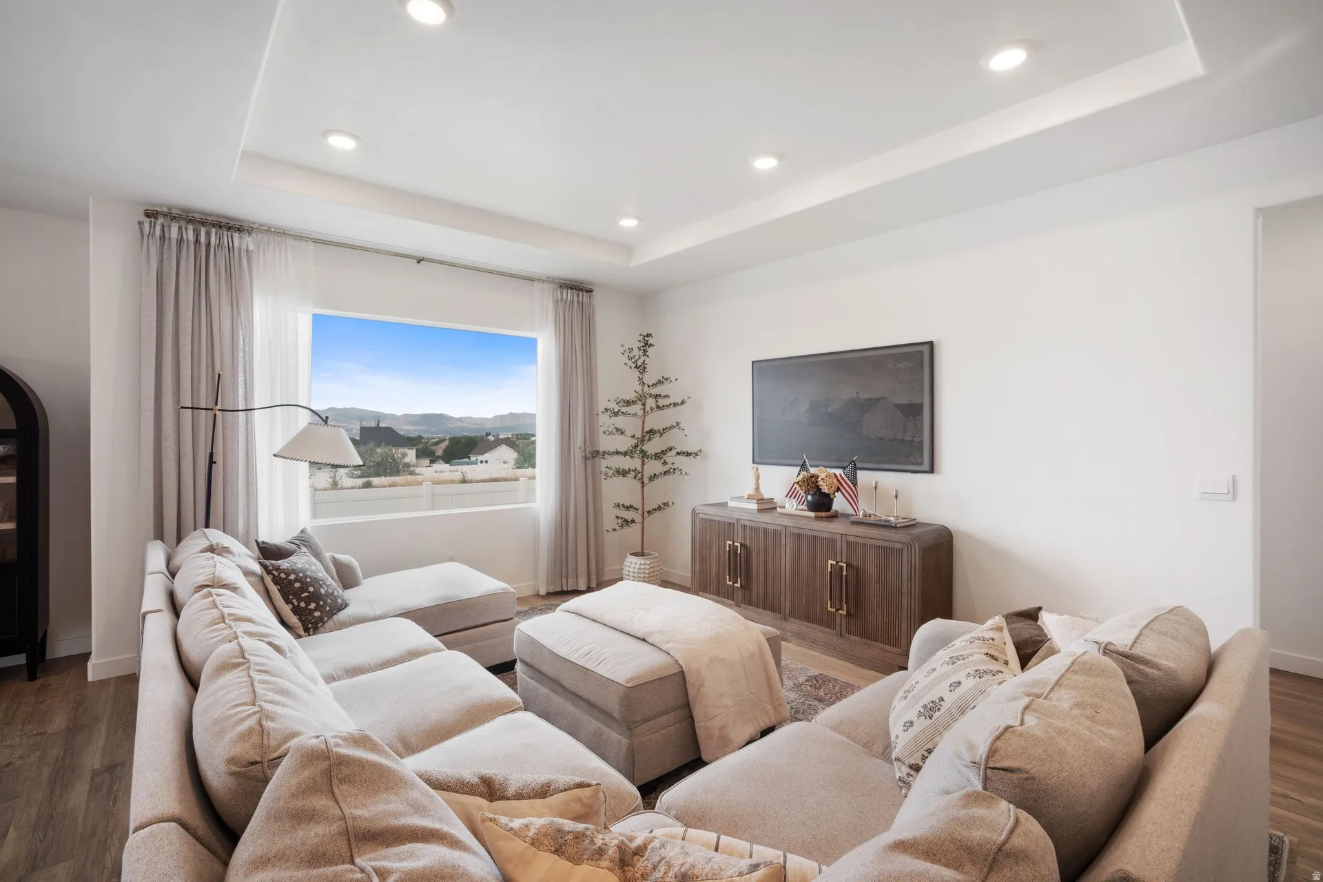 Spacious living area featuring a large picture window, recessed lighting, tray ceiling, and wood-finish flooring