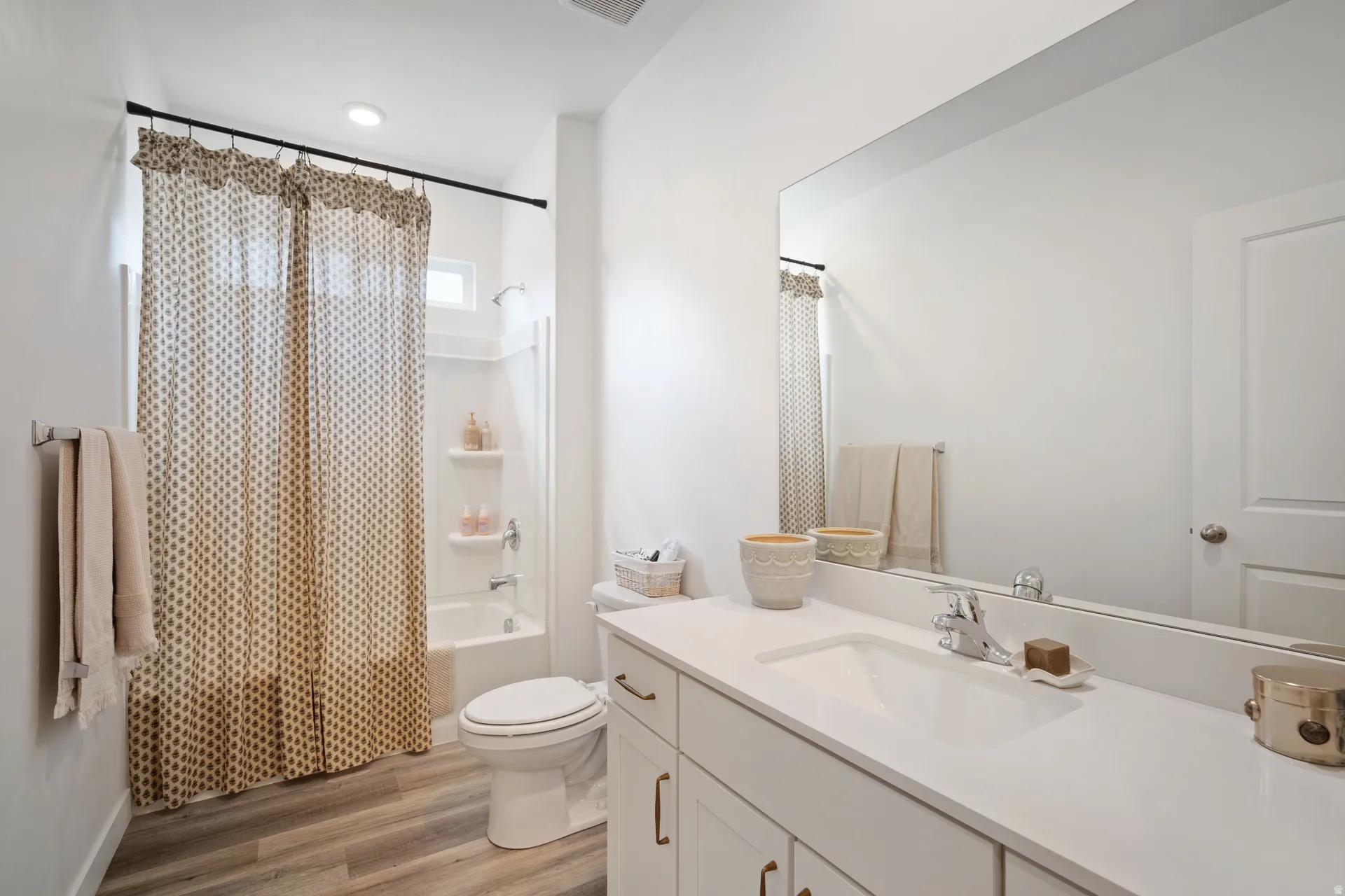 Bathroom featuring a single vanity with an integrated sink, a large wall-mounted mirror, and a full-size tub with an overhead shower and built-in shelving