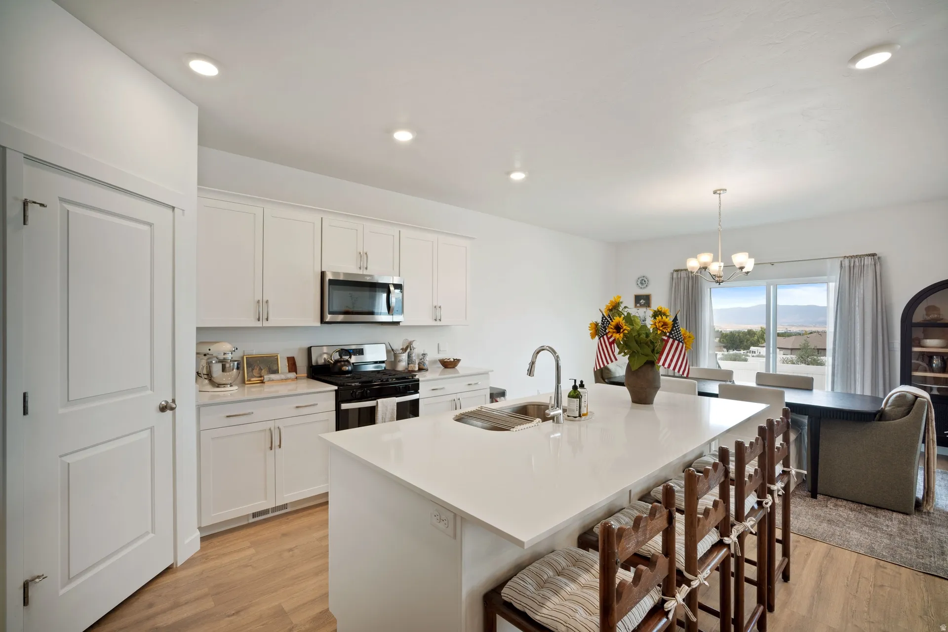 Bright kitchen featuring white cabinetry, a large kitchen island with integrated sink, stainless steel appliances, and wood-finish flooring