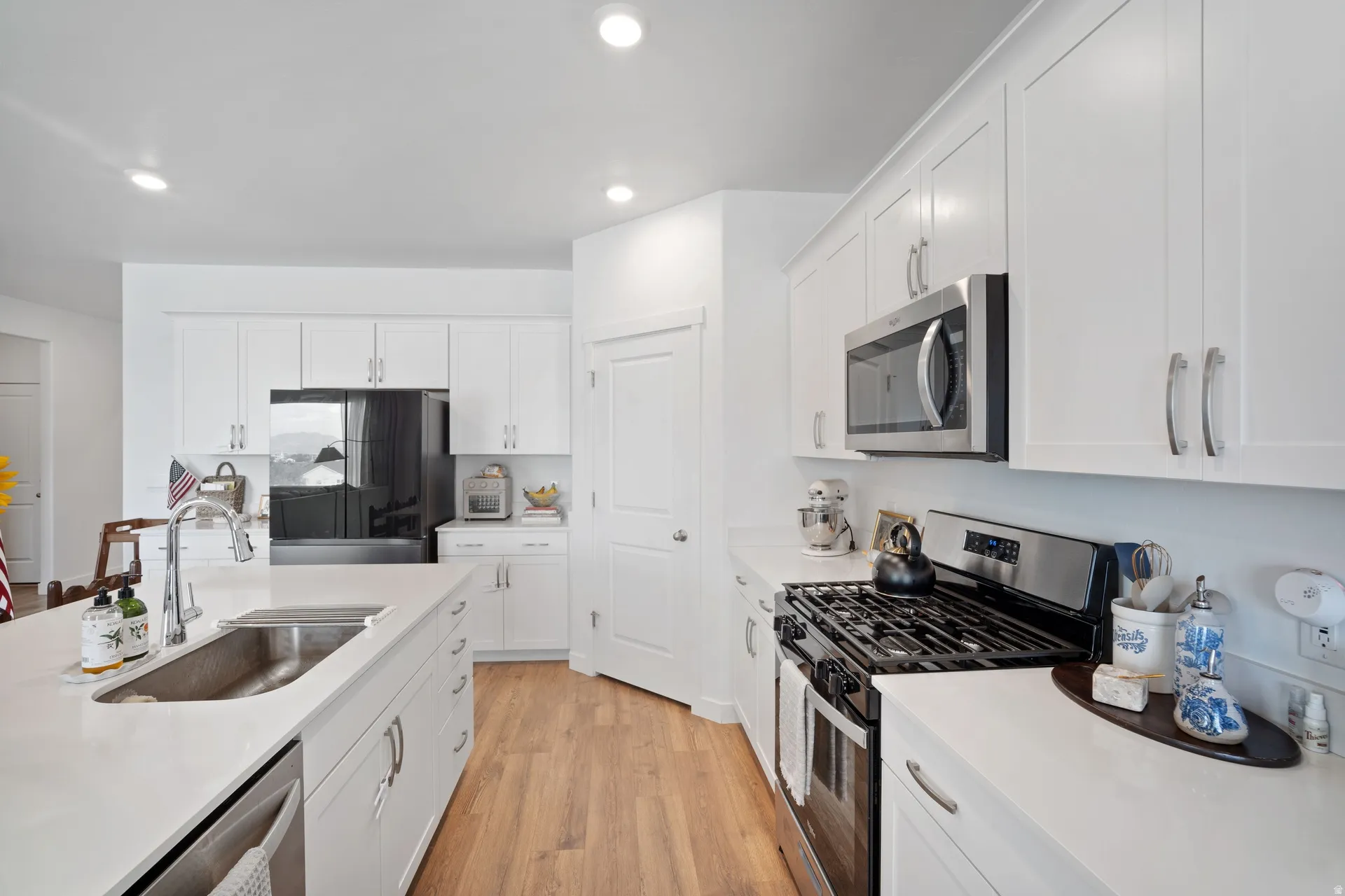 Modern kitchen featuring white cabinetry, light countertops, wood-finish flooring, stainless steel appliances, and an island with an undermount sink