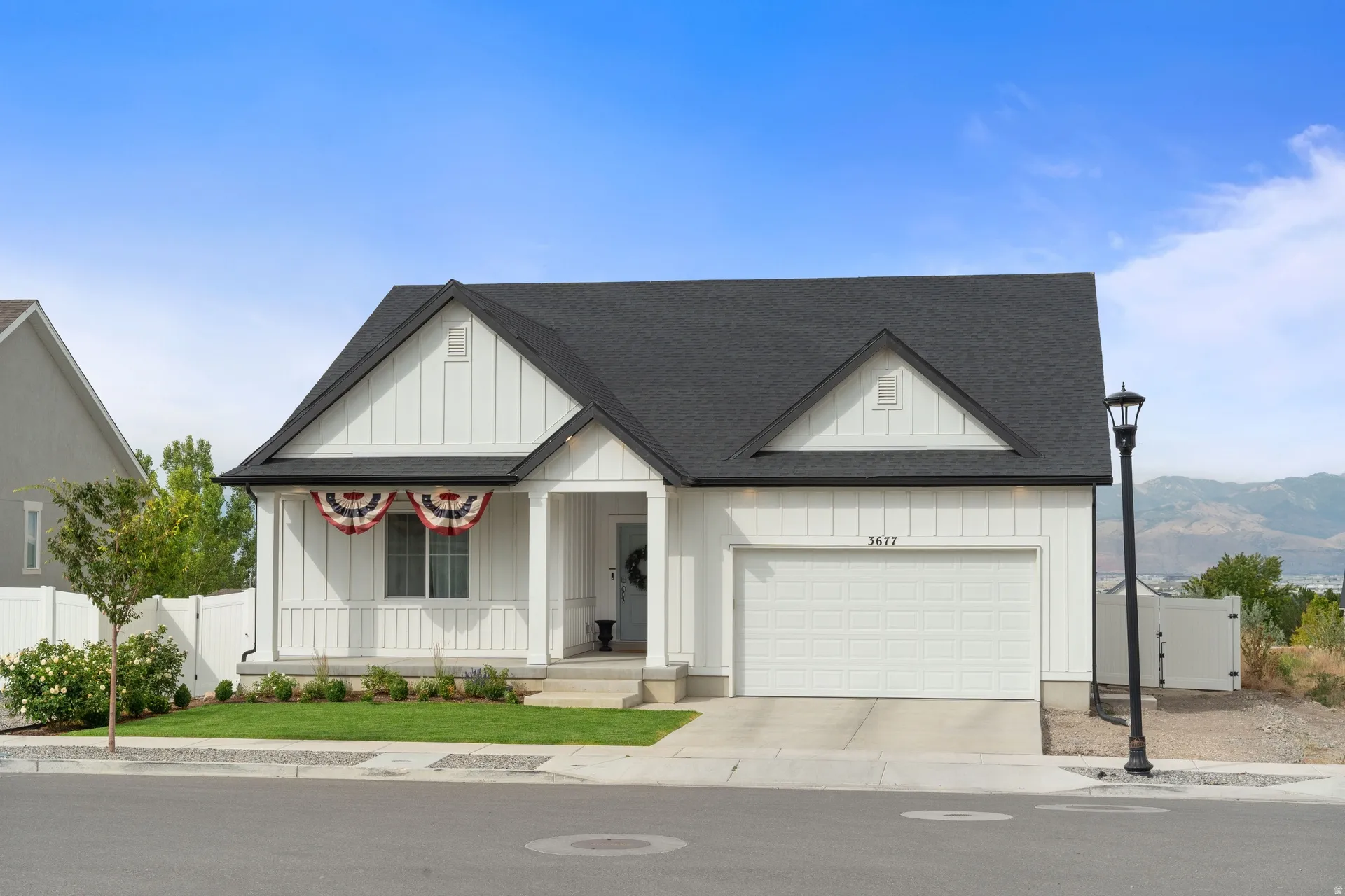 Contemporary white residence featuring board and batten siding, a black asphalt shingle roof, an integrated single-car garage, a covered front porch, and a manicured front lawn