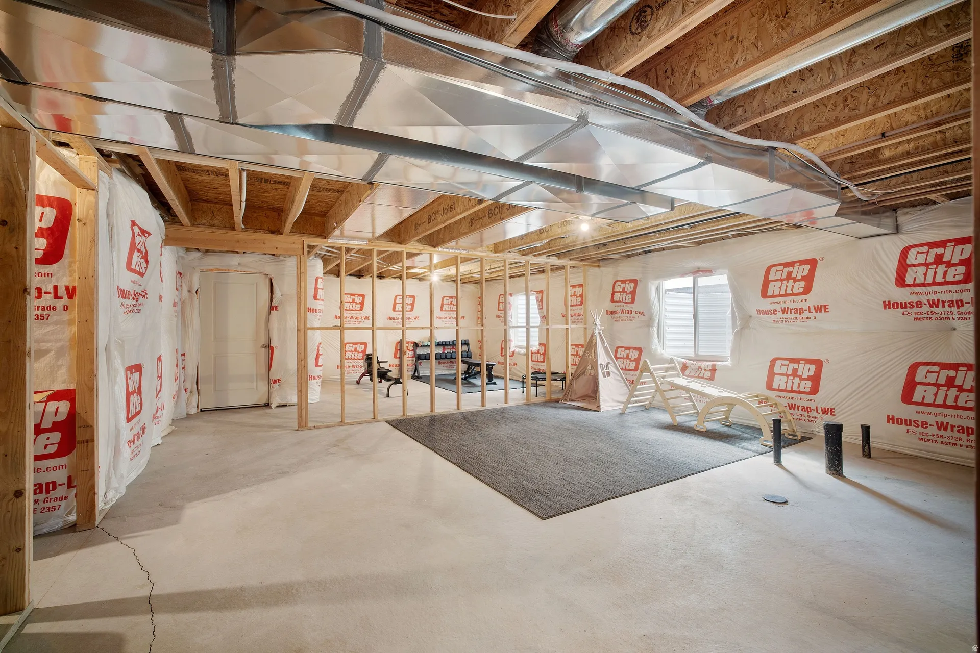 Unfinished basement featuring exposed wood framing, concrete flooring, and an egress window