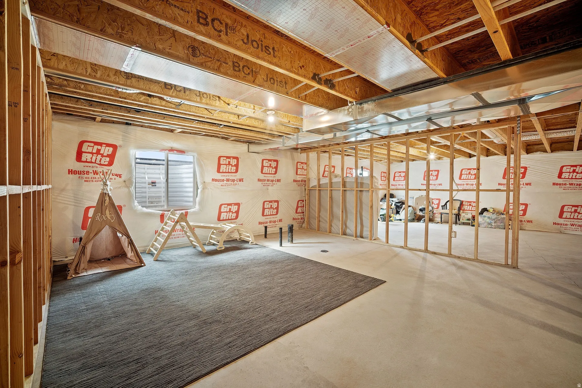 Unfinished basement with exposed wood framing, an egress window, and visible HVAC ductwork