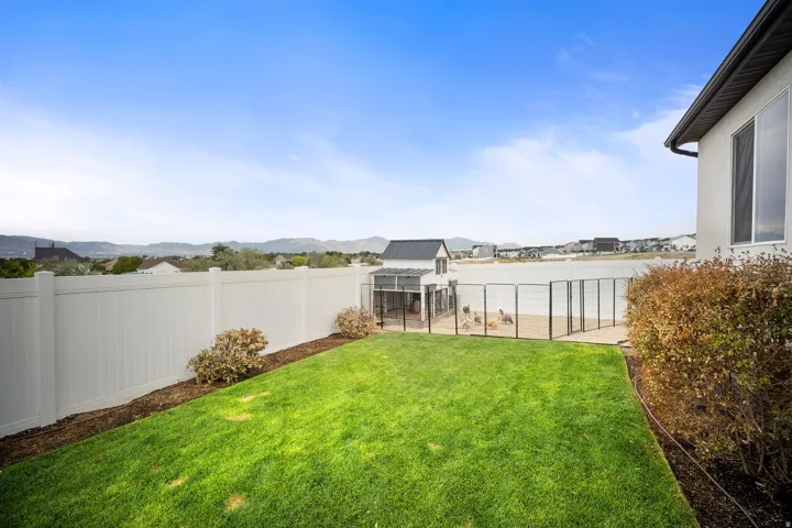 Expansive backyard featuring a manicured lawn, white privacy fencing, and established shrubbery