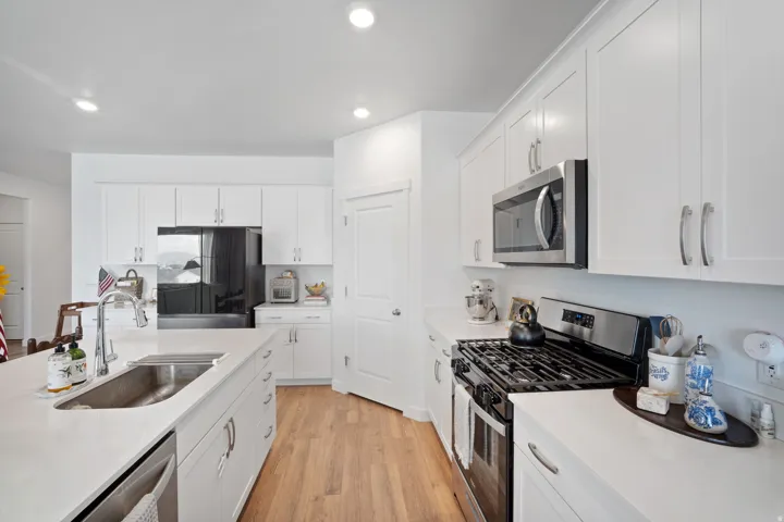 Modern kitchen featuring white cabinetry, light countertops, wood-finish flooring, stainless steel appliances, and an island with an undermount sink