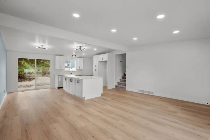 Open-concept living space featuring wood-finish flooring, recessed lighting, and a modern kitchen island with white shaker cabinetry