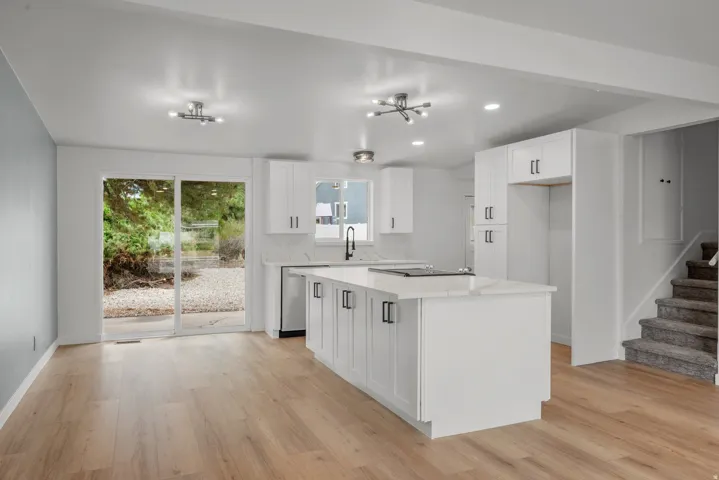 Open concept kitchen featuring an expansive center island with seating, white shaker cabinetry, and light wood-finish flooring
