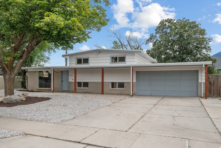 Split-level residence featuring a light gray garage door, brick and white siding exterior, and a gravel front yard
