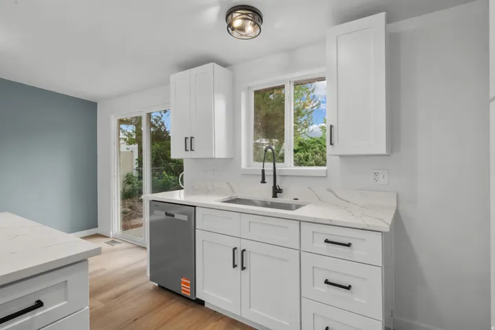 Kitchen area featuring white shaker cabinetry, quartz countertops, a stainless steel sink with a matte black faucet, and wood-finish flooring