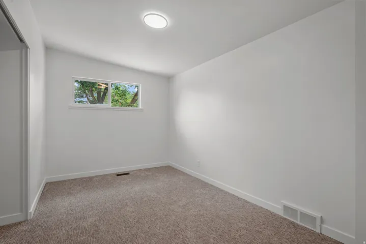 Room featuring neutral-toned carpet, white walls, and a single window with exterior tree foliage visible