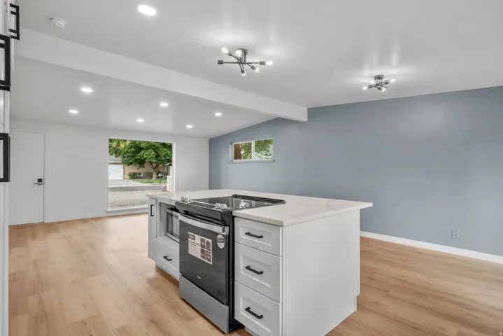 Kitchen island with a built-in range and microwave, white cabinetry, light-toned countertops, and black hardware