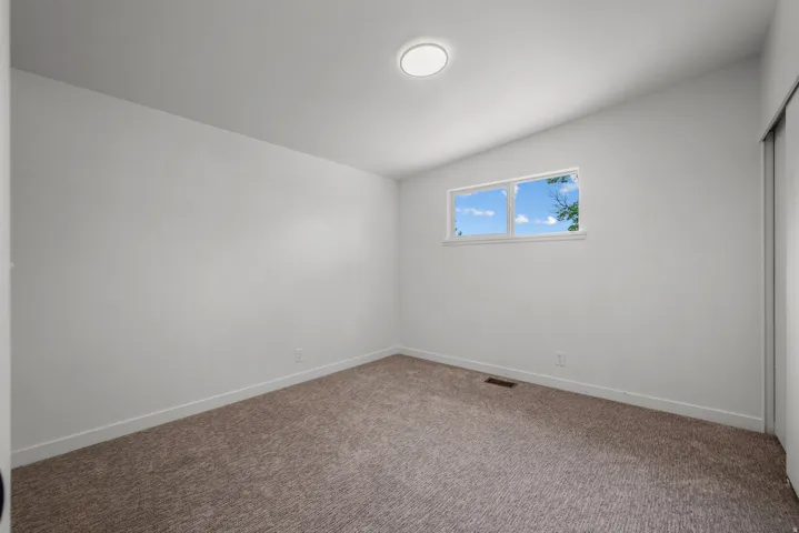 Bedroom featuring neutral carpeting, white walls, a single window, ceiling-mounted lighting, and a closet with sliding doors