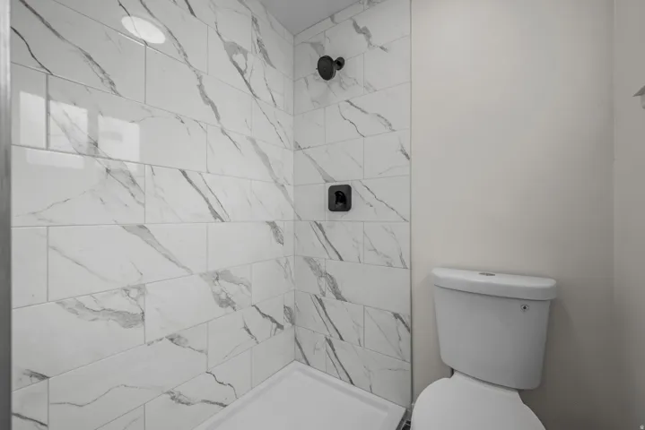 Shower enclosure featuring white marble-look subway tile and matte black fixtures
