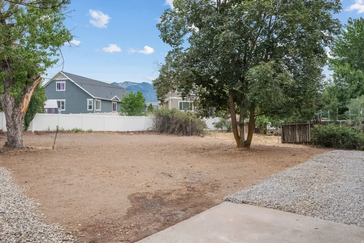 Spacious outdoor area featuring a large gravel section, mature trees, and a concrete pad