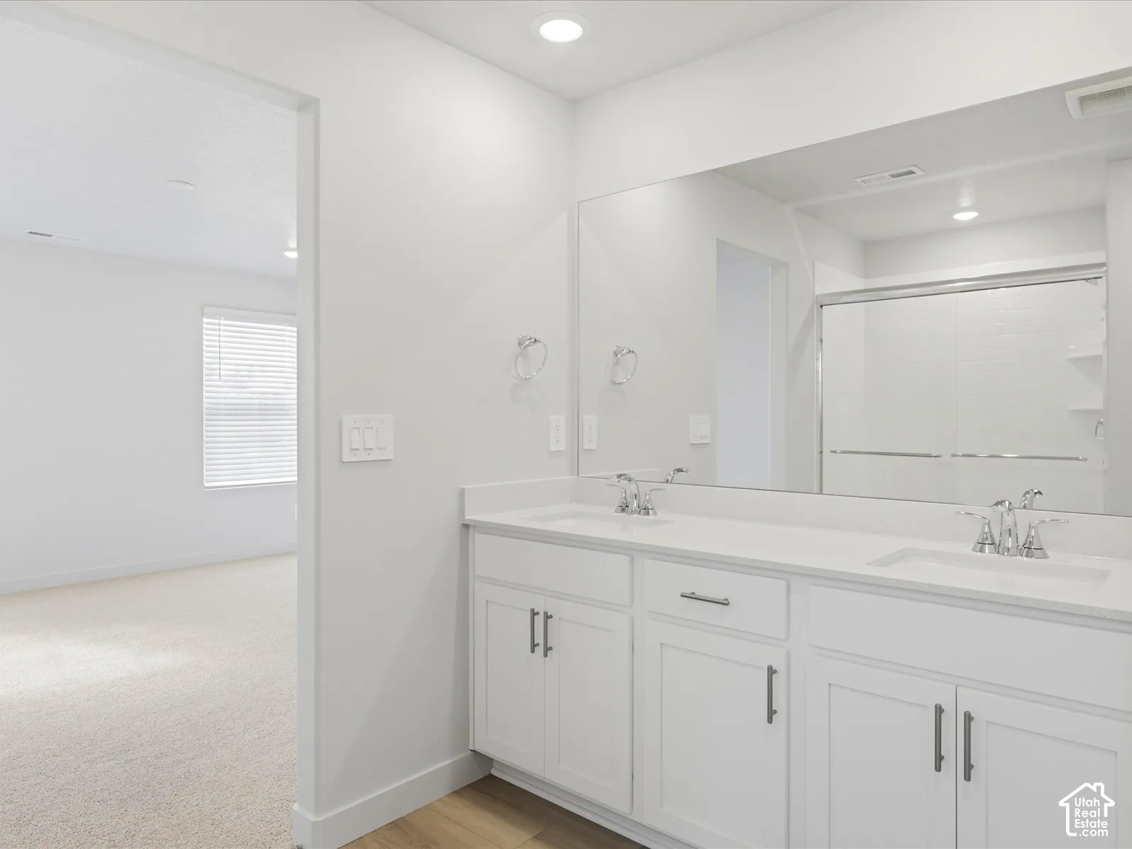 Dual-sink vanity with white cabinetry, light-toned countertop, and recessed lighting, featuring a large wall-mounted mirror and a shower with a sliding glass enclosure