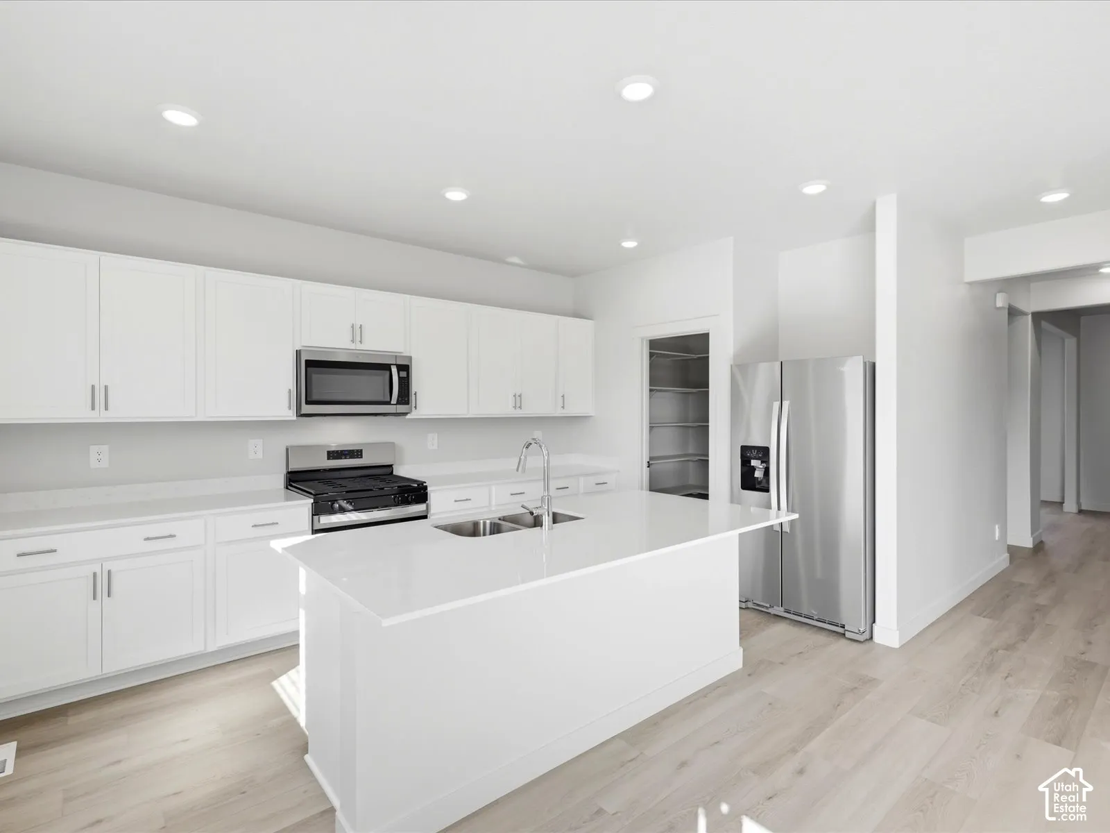 Kitchen featuring white cabinetry, quartz countertops, a central island with a double-basin sink, wood-finish flooring, and stainless steel appliances
