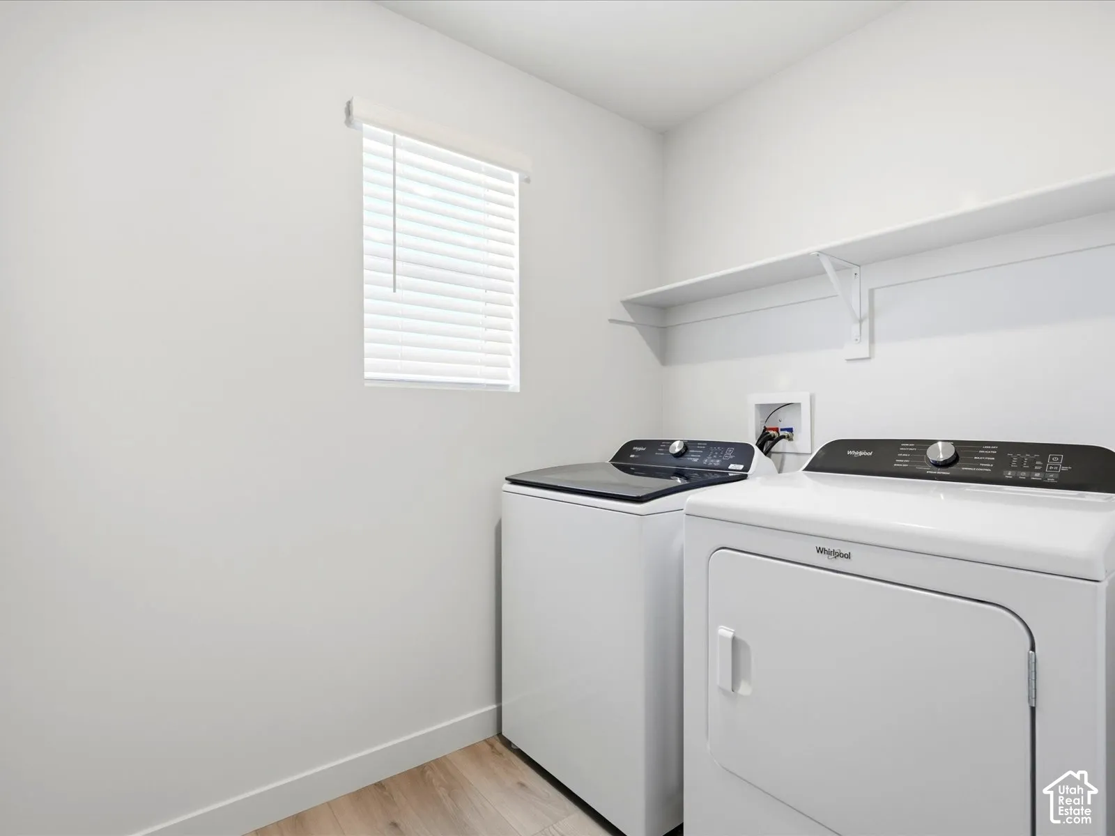 Laundry room featuring wood-finish flooring, a wall-mounted shelving unit, and a window with horizontal blinds