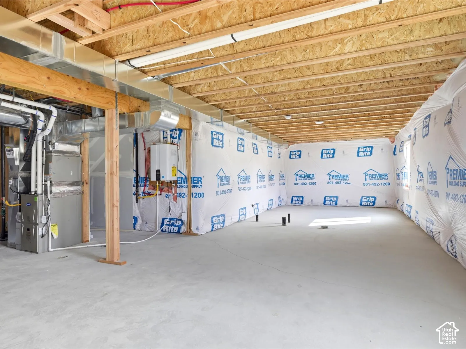 Unfinished lower level featuring exposed wood joist ceilings, concrete flooring, foundation wall vapor barriers, and installed HVAC and tankless water heating systems
