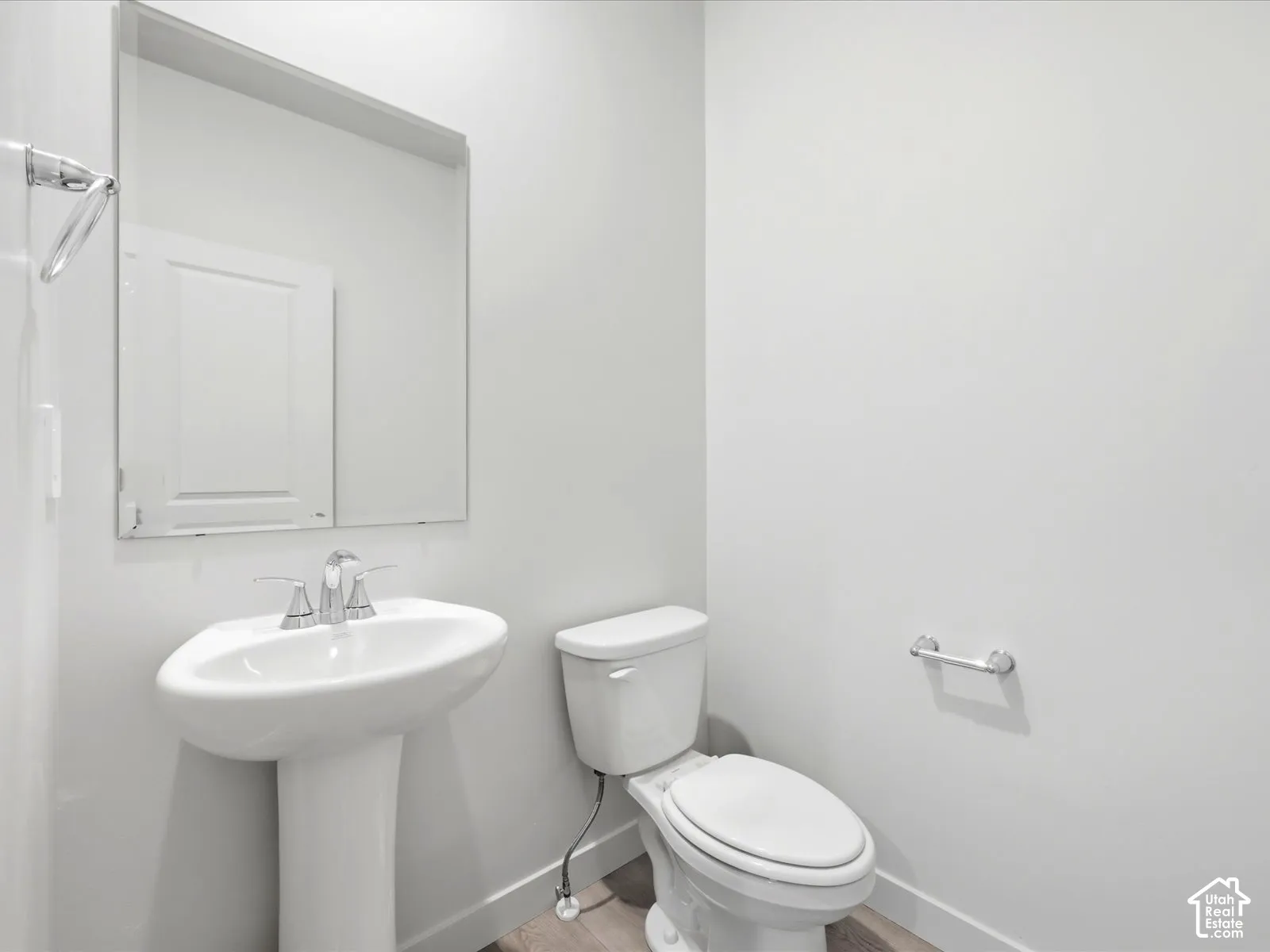 Pedestal sink with a polished chrome faucet, rectangular wall-mounted mirror, white ceramic toilet, and chrome hardware