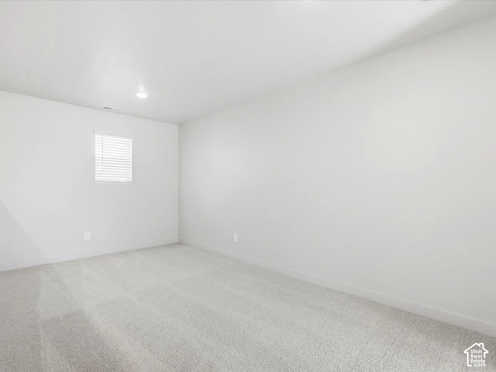 Neutral-toned carpeting, smooth wall finishes, recessed ceiling lighting, and a single-pane window featuring integrated horizontal blinds