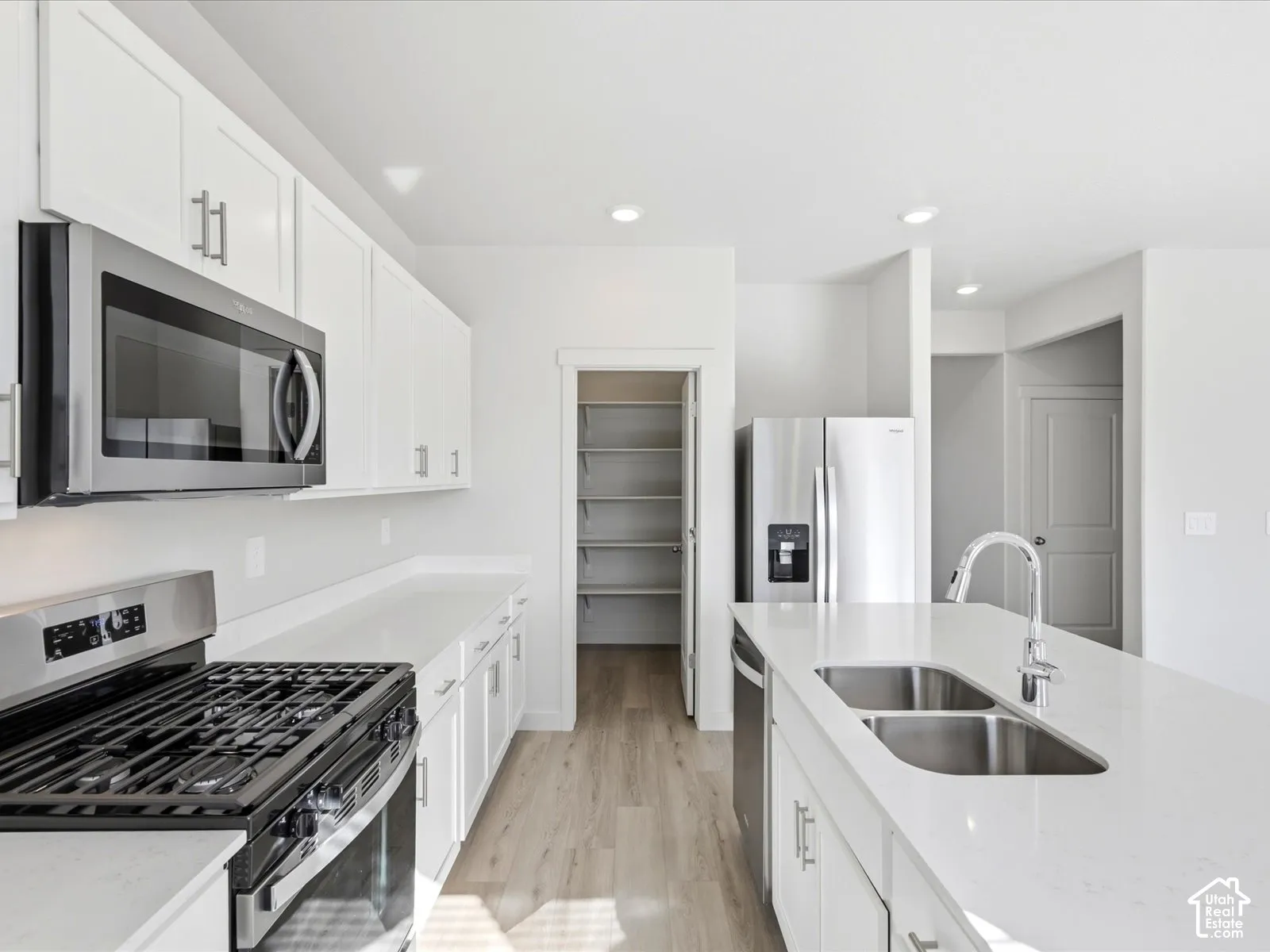 Kitchen featuring white cabinetry, quartz countertops, stainless steel appliances, a center island with a dual-basin stainless steel sink, and a walk-in pantry