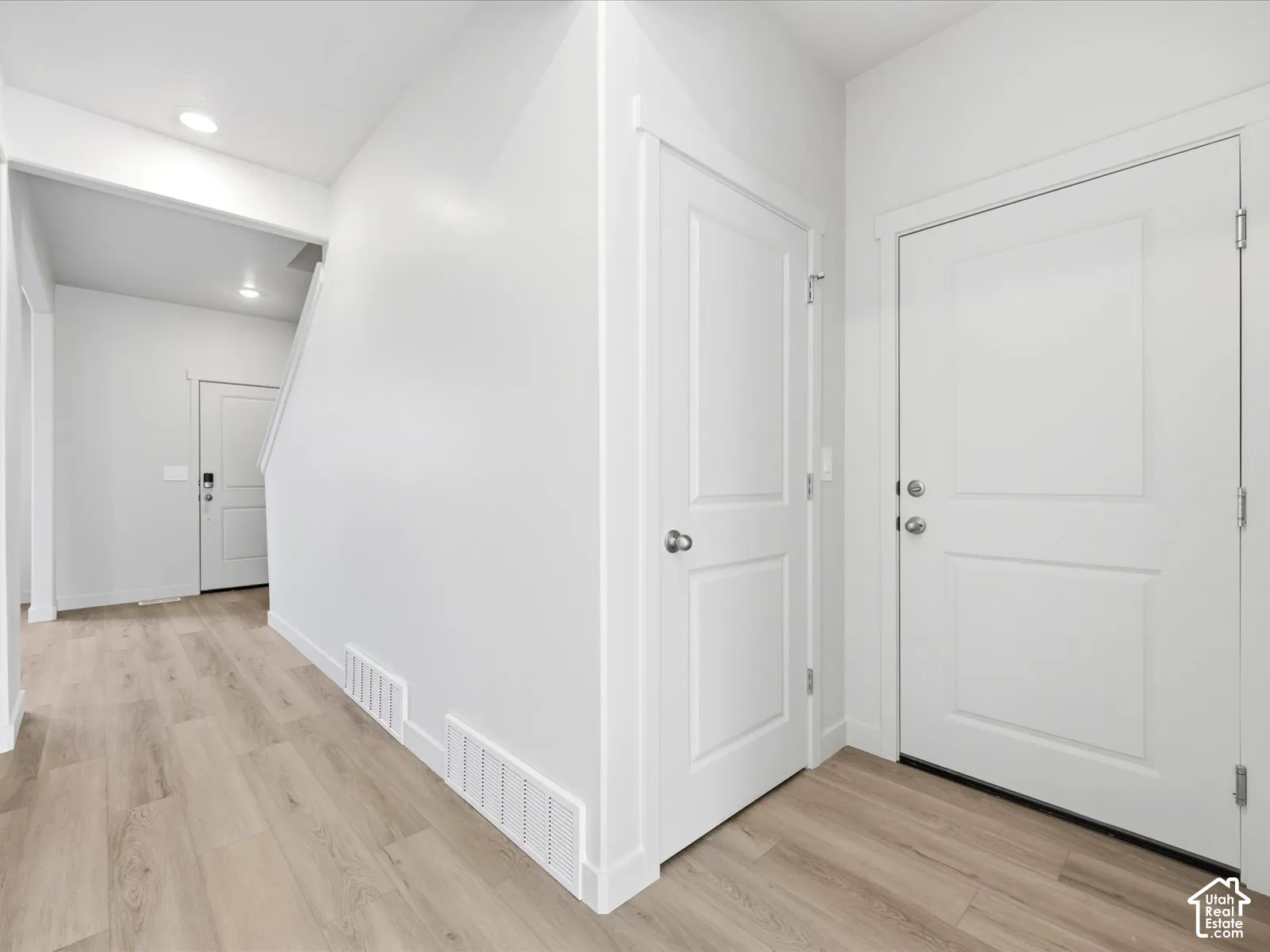 Interior entryway featuring light wood-finish flooring, crisp white walls, recessed ceiling lighting, and solid-core panel doors