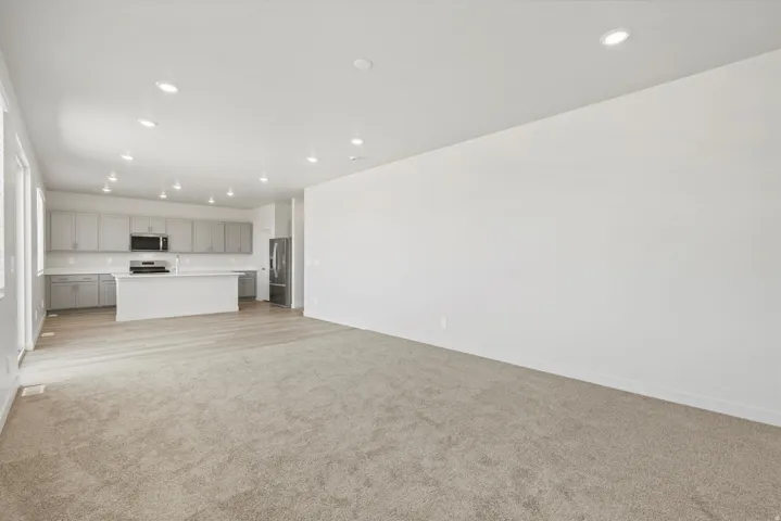 **DISCLAIMER** Interior package may vary. Open-concept living area featuring recessed lighting, a neutral color palette, light-toned carpeting, and wood-finish flooring
