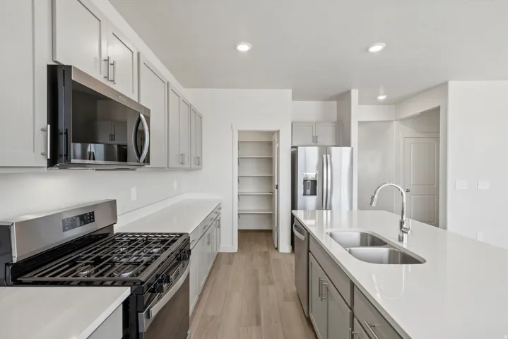 **DISCLAIMER** Interior package may vary. Contemporary kitchen featuring light gray cabinetry, stainless steel appliances, white countertops, and wood-finish flooring