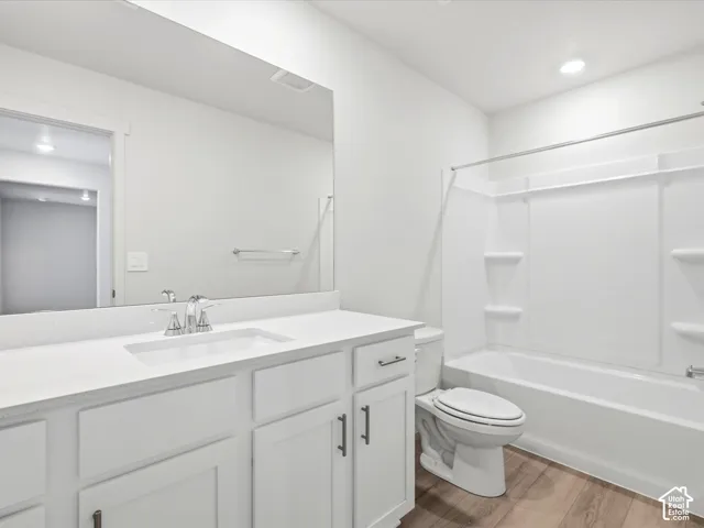 Bathroom featuring white cabinetry, solid-surface countertop with integrated sink, chrome hardware, full-width vanity mirror, and tub-shower combination with surround