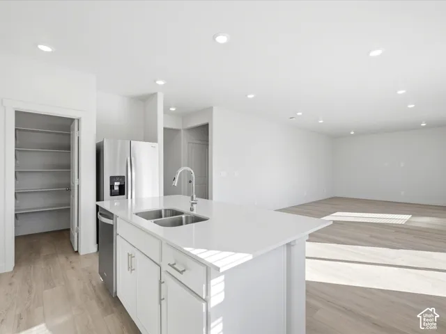 Kitchen featuring a center island with a stone-surface countertop, stainless steel sink with a high-arch faucet, white cabinetry, integrated stainless steel appliances, and wood-finish flooring