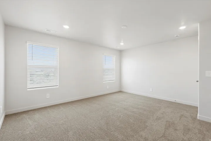 **DISCLAIMER** Interior package may vary. Spacious room featuring neutral carpeting, white walls, two windows with blinds, recessed ceiling lighting, and white baseboards