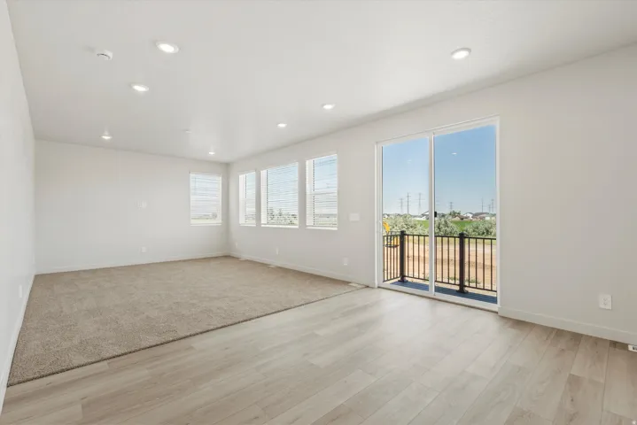 **DISCLAIMER** Interior package may vary. Open-concept room featuring light wood-finish flooring, recessed lighting, and a sliding glass door leading to a balcony with black railings