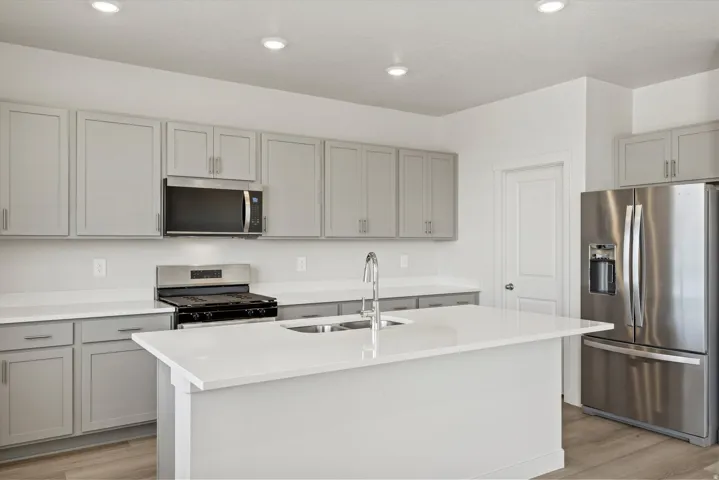 **DISCLAIMER** Interior package may vary. Modern kitchen featuring a central island with an undermount sink, light-toned cabinetry, stainless steel appliances, recessed lighting, and wood-finish flooring