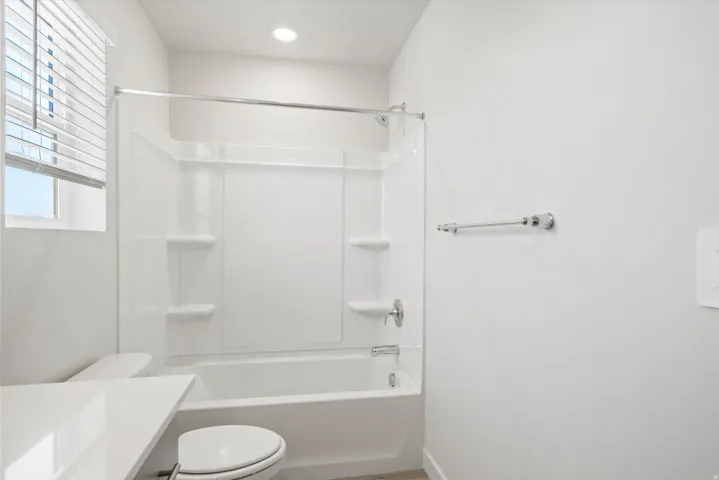 **DISCLAIMER** Interior package may vary. Bright bathroom featuring a white tub and shower combination with integrated shelving, a window with horizontal blinds, recessed lighting, and a chrome towel bar