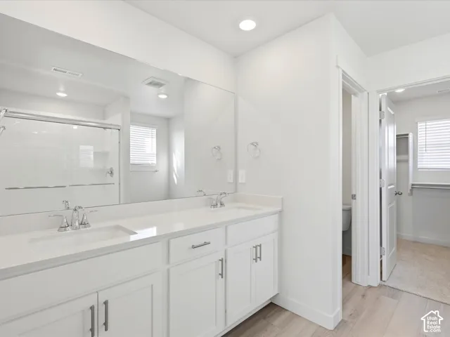 Double vanity with integrated sinks, white cabinetry, polished hardware, a full-width mirror, and wood-finish flooring