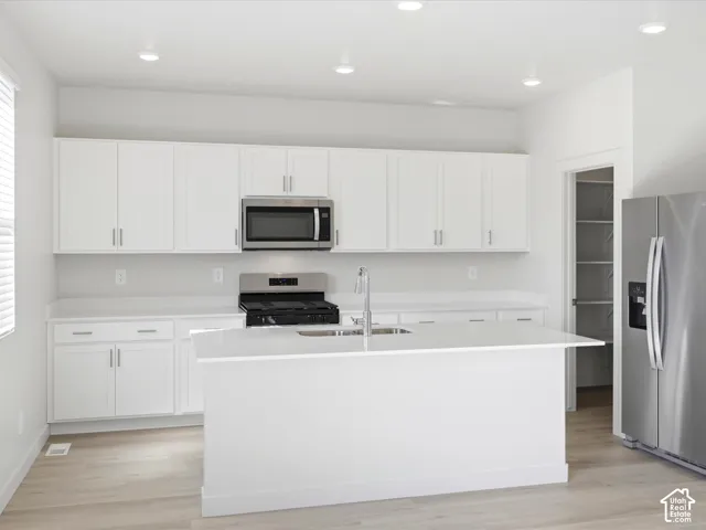 Kitchen featuring white shaker-style cabinetry, quartz countertops, stainless steel appliances, a central island with an integrated sink, and wood-finish flooring