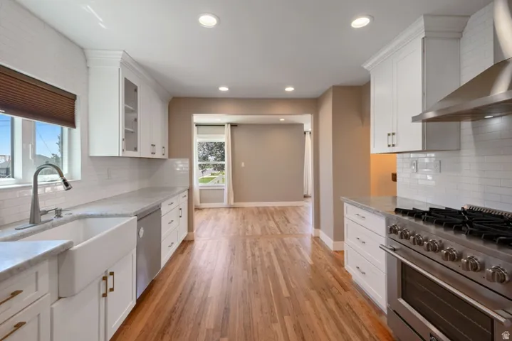Modern kitchen featuring newer white shaker cabinetry, new commercial gas range, newer refrigerator and dishwasher, a subway tile backsplash, light-toned countertops, and wood-finish flooring