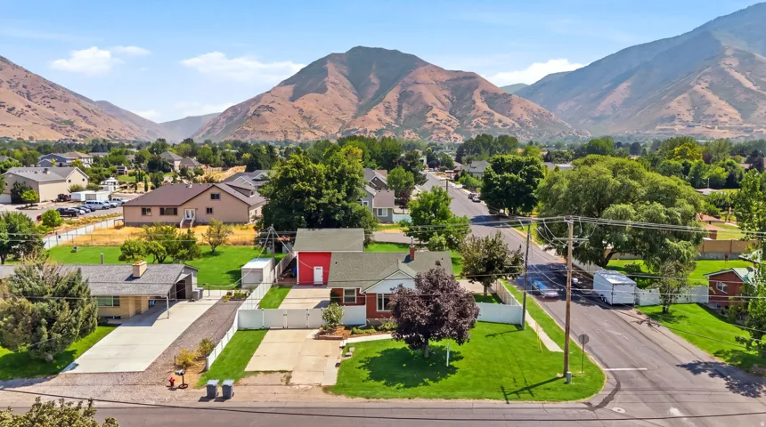 Mountain backdrop with a residential setting featuring a red-sided structure, green lawns, and mature trees
