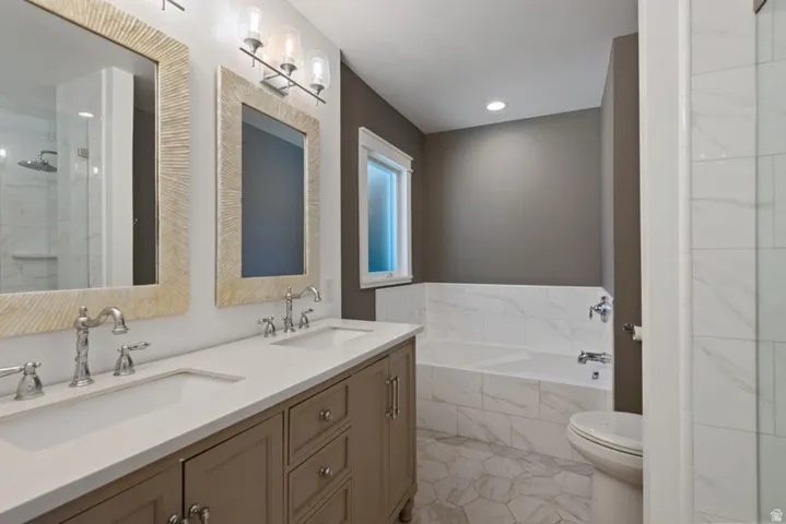 Primary En-Suite Bathroom featuring a double vanity with stone countertops, a tiled soaking tub, an enclosed glass shower, and tile floors