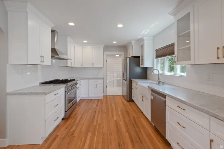Modern kitchen featuring newer white shaker cabinetry, new commercial gas range, newer refrigerator and dishwasher, a subway tile backsplash, light-toned countertops, and wood-finish flooring