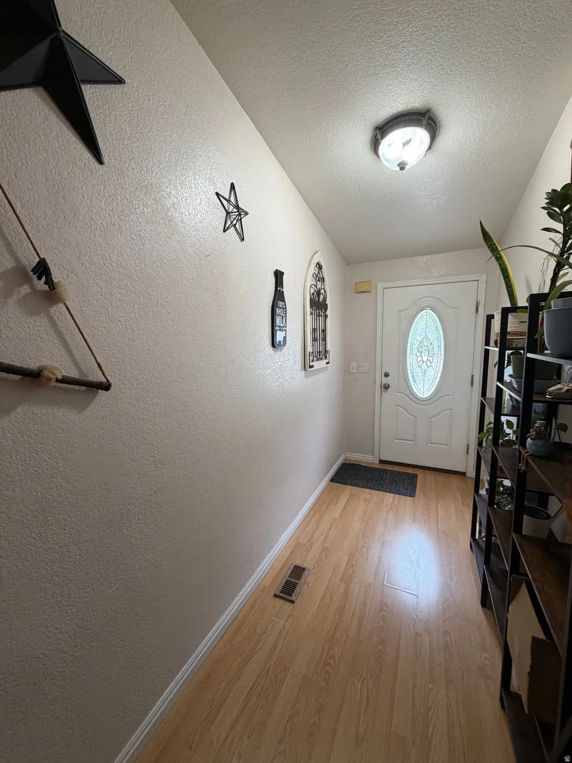 Entryway featuring wood-finish flooring, textured walls, a white front door with an oval glass insert, and a flush-mount ceiling light fixture