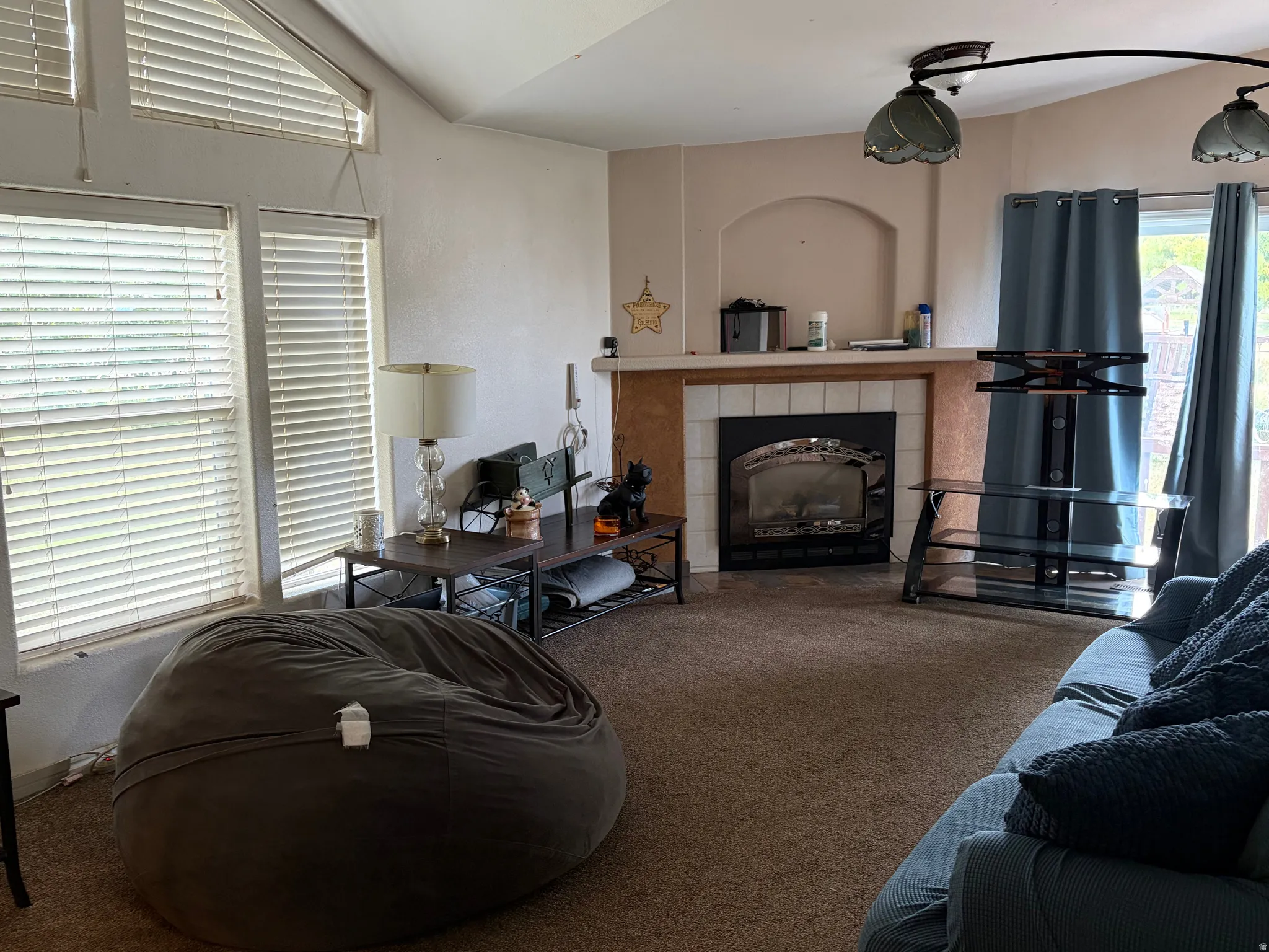 Living area featuring a fireplace with a tile surround and hearth, vaulted ceilings, and large windows with blinds