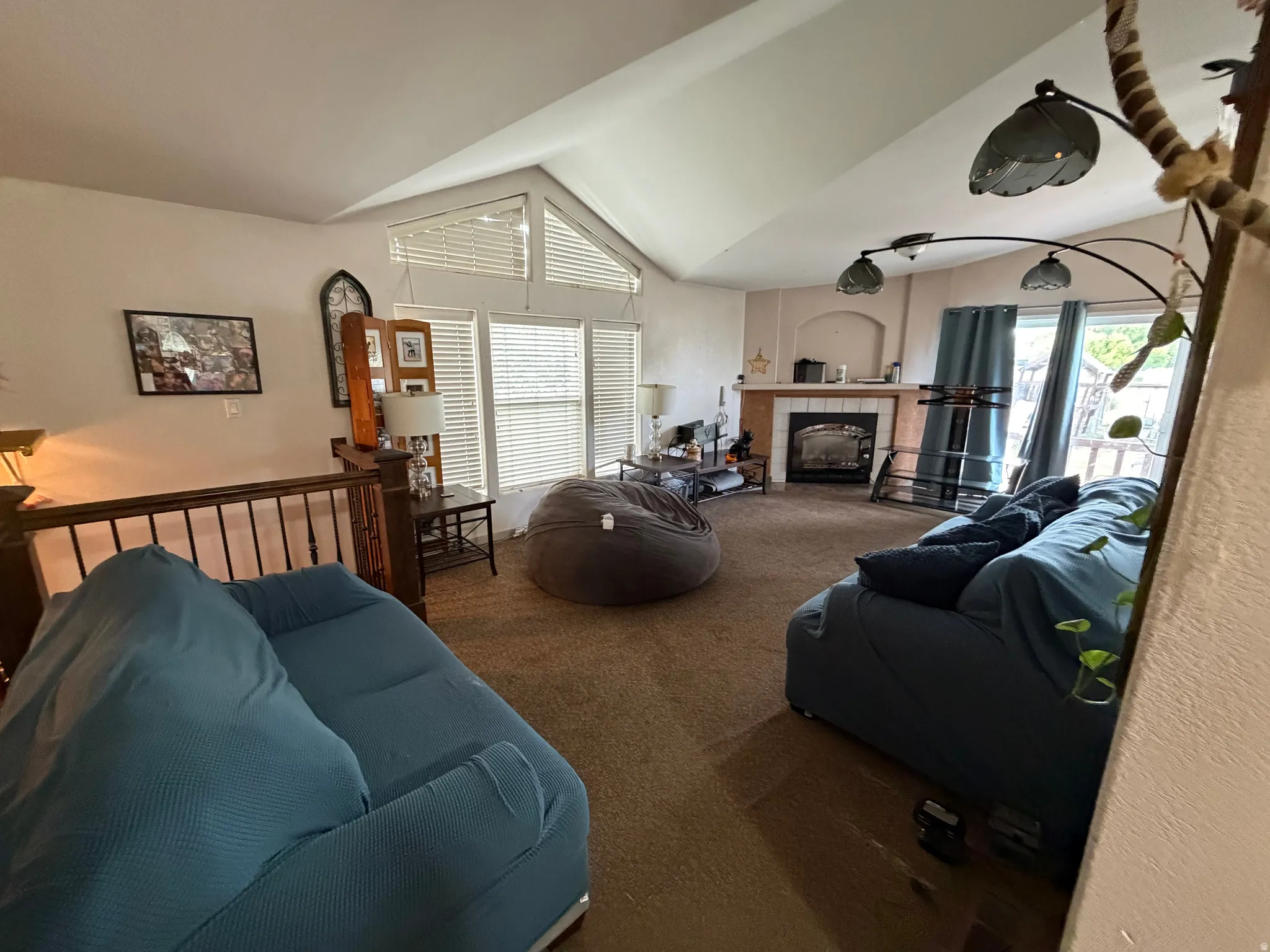 Vaulted ceilings enhance this living space featuring abundant natural light from multiple windows, a gas fireplace with a wood mantel, and a railing overlooking a lower level