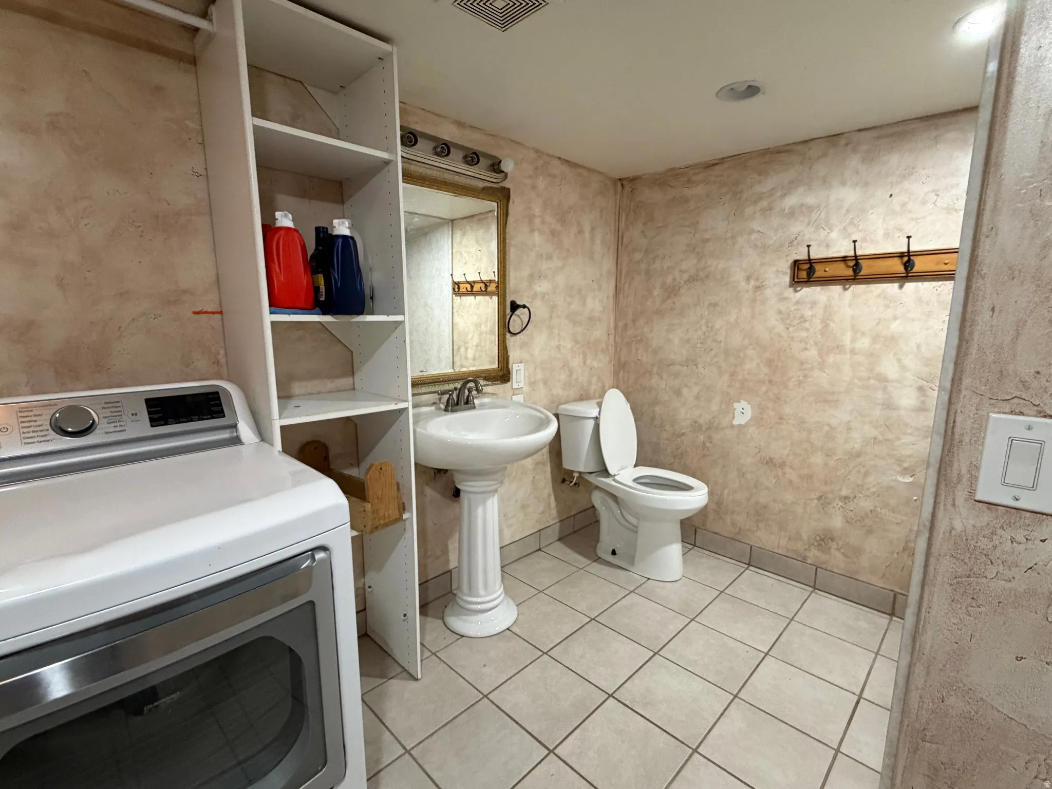 Pedestal sink with mirror, commode, tiled flooring, wood-finish wall hooks, and built-in shelving
