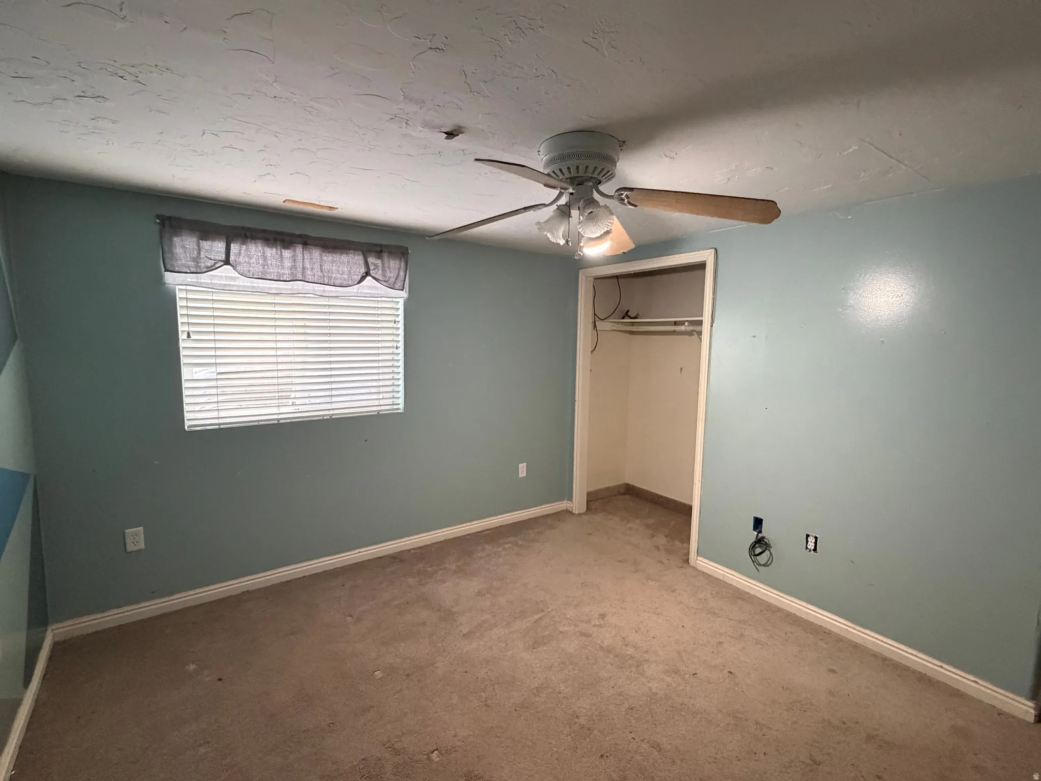 Interior room featuring light-colored carpet flooring, a window with horizontal blinds, and a ceiling fan with integrated lighting