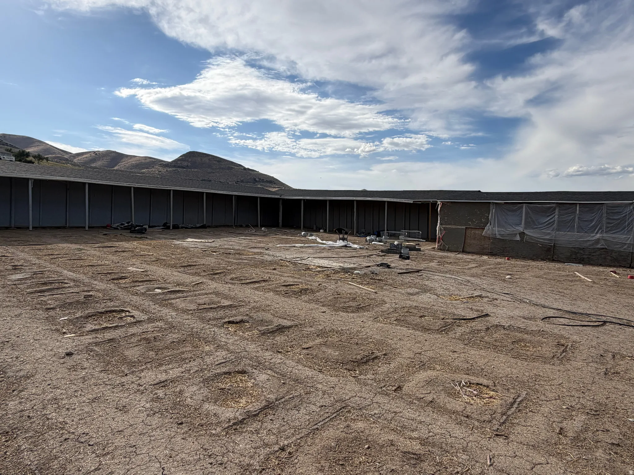 Expansive level lot with a structure featuring a dark shingled roof and light-colored siding, set against a backdrop of distant hills