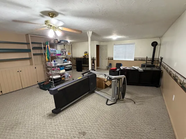 Spacious carpeted room featuring built-in cabinetry, shelving, and a ceiling fan with integrated lighting