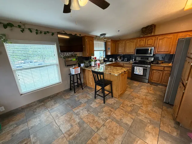 Spacious kitchen featuring wood cabinetry, stainless steel appliances, a center peninsula with granite countertop, and tile flooring