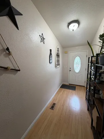 Entryway featuring wood-finish flooring, textured walls, a white front door with an oval glass insert, and a flush-mount ceiling light fixture